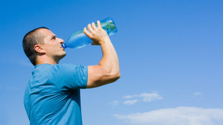 Person trinkt frisches Wasser aus einer Flasche im Freien